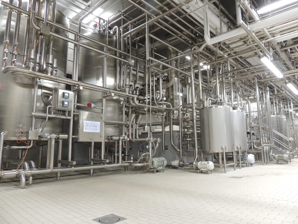 An image showcasing meticulously installed stainless steel hygienic piping systems and tanks by JBT A&B Process Systems, within a food and beverage production facility.